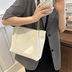 Borsa tote bianco crema con catena dorata indossata su un abito grigio da donna