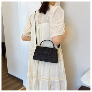 Close-up of a sparkling black sequin crossbody bag styled with a white lace dress