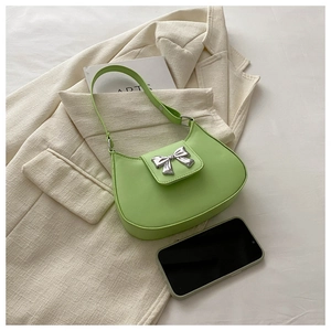 Mini green shoulder bag with silver bow detail shown next to a smartphone for size reference