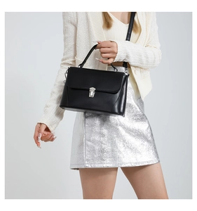 Detail of a black crossbody bag with silver buckle worn by a model in a shiny dress