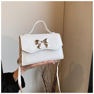Detailed shot of white crossbody bag with large gold bow buckle and saffiano texture