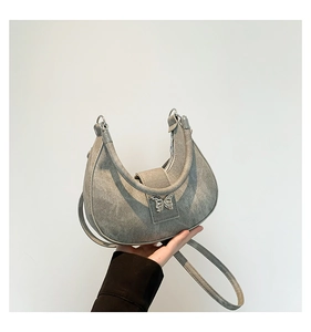 Détail du sac demi-lune argenté avec texture cuir vintage et fermoir papillon métallique