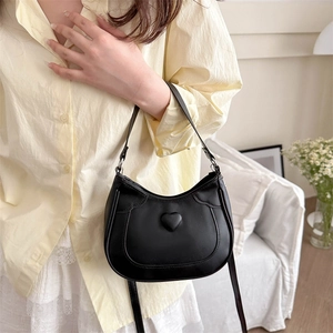 Fashionable black heart-shaped shoulder bag shown in a stylish lifestyle setting