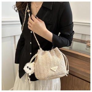 Detail of woven straw bucket bag featuring a cute plush monster charm and chain strap