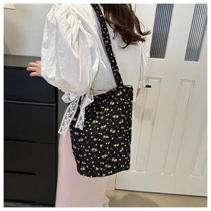 Rear view of a black floral tote bag with a white lace bow strap worn by a model