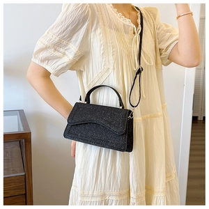 Detail of a black sequin crossbody bag with glitter texture and curved flap design