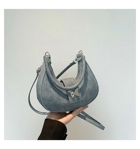 Gros plan d'un sac demi-lune bleu avec boucle papillon argentée et bandoulière chaîne