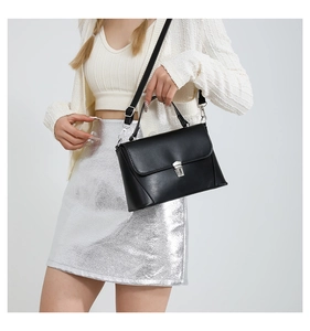Close-up of black crossbody bag with silver square lock on a textured white outfit