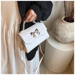Close-up of white leather crossbody bag with a gold bow buckle and top handle