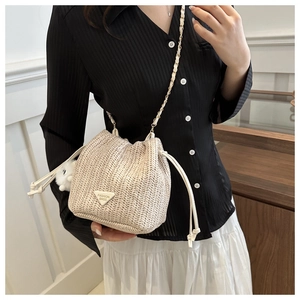 Detail shot of beige woven bucket bag with drawstring closure and golden chain strap