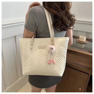 Detail of off-white quilted tote bag with V-pattern stitching and pink plush monster charm