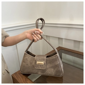 Detail of a brown suede baguette bag featuring a gold buckle and elegant top handle strap