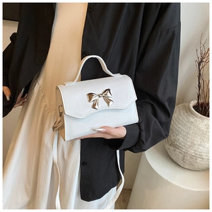 White leather crossbody bag featuring gold metal bow clasp held at waist level