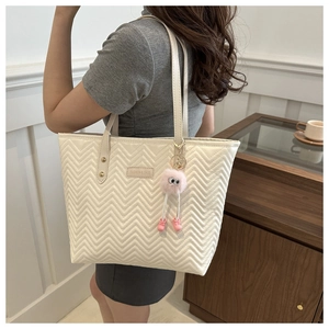 Close-up of cream quilted tote bag with zigzag pattern and pink plush monster charm