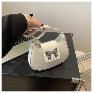 Detail of white half-moon bag featuring a silver metal bow buckle and smooth leather