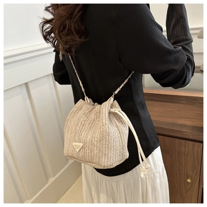 Detailed view of beige straw bucket bag featuring fine V-shaped woven texture and chain strap