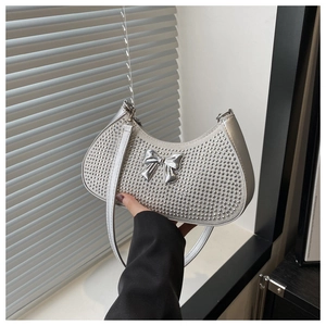 Detail of silver rhinestone crescent bag with metallic bow held by hand
