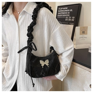 Close-up of black pleated crescent bag featuring silver butterfly charm and knotted strap