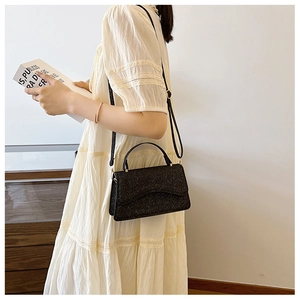 Close-up of glittery black crossbody bag with gold hardware worn by a model