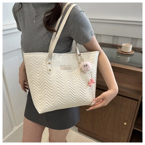 Detail of white quilted tote bag featuring fashion metal logo and pink plush charm