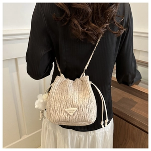 Detail of beige woven straw bucket bag with drawstring closure and chain strap