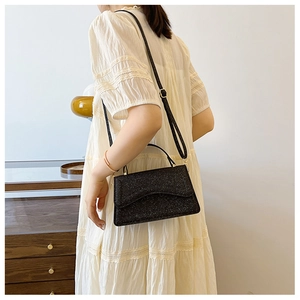 Detail of elegant black sequin crossbody bag styled with a white layered lace dress