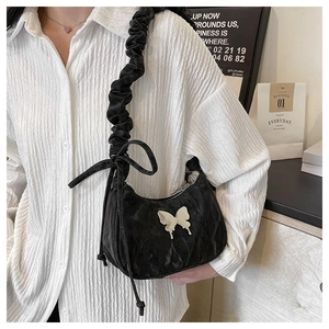 Detail of a black ruffled strap shoulder bag featuring a silver butterfly ornament
