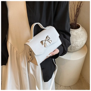 Close-up of white PU leather crossbody bag with silver bow accent and lychee texture