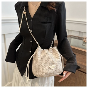 Detail of straw bucket bag with gold chain strap and drawstring closure in beige