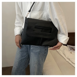 Detail of black leather envelope bag with a rectangular cutout handle and golden hardware