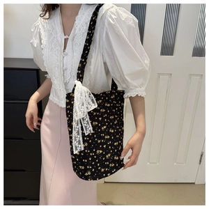 Detail of black quilted tote bag featuring yellow floral patterns and a large lace bow