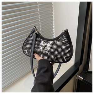 Detail of black leather crescent bag featuring silver studs and a 3D metallic bow accent