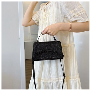 Close-up of black sequined handbag with gold hardware and adjustable strap on a model