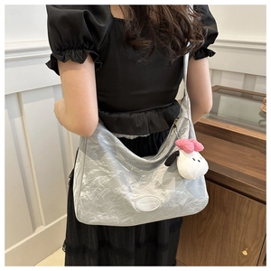 Détail d'un sac hobo argenté à texture plissée avec un charmant pendentif en peluche