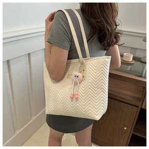 Close-up of beige quilted tote bag with wavy stitching and a cute pink plush charm