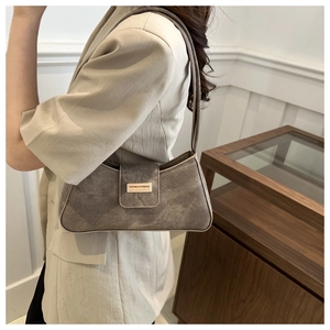 Detail of taupe baguette bag with matte texture and metallic buckle on model shoulder