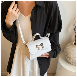 Close-up of white crossbody bag with silver bow ornament on minimalist display