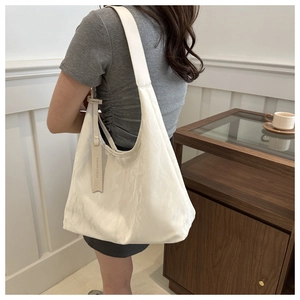 Détail d'un grand sac bandoulière blanc à texture plissée porté par un mannequin