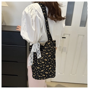 Detail of black floral tote bag with quilted texture and decorative lace bow