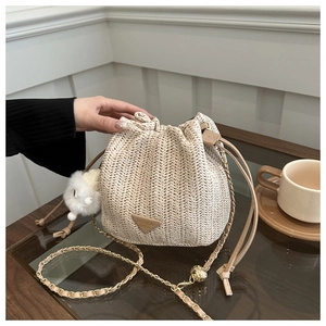 Detail view of woven straw bucket bag featuring a triangle leather patch and plush charm