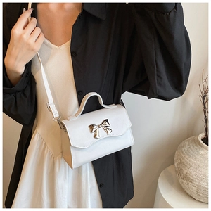 Chic white crossbody bag featuring a golden bow buckle shown on a model