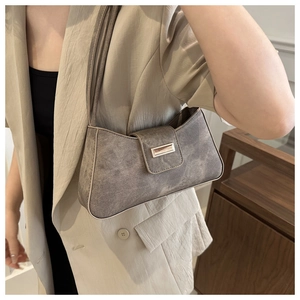 Detail of taupe baguette bag with matte texture and metal buckle on female shoulder