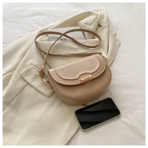 Detail of beige saddle bag with gold metal buckle and adjustable strap on a minimalist set