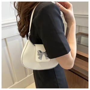 Detailed side view of white crescent saddle bag with silver bow on model in black outfit