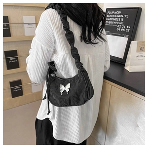 Detail of black pleated shoulder strap and silver butterfly buckle on a textured hobo bag