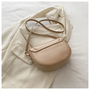 Detail of beige leather saddle bag with gold metal buckle on a white blazer