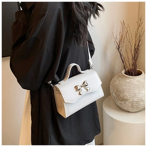 Detail of white crossbody bag with fine texture and gold bow buckle worn by a model