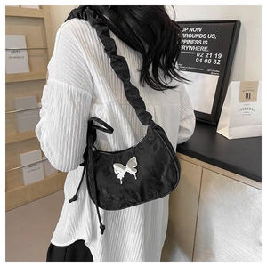 Detail of black crescent shoulder bag with silver butterfly and ruched strap on model
