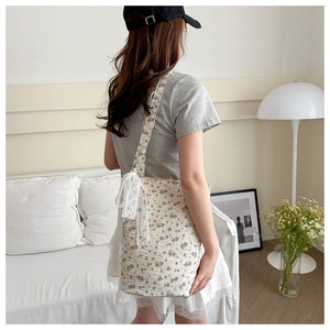 Lace bow detail and floral pattern on cream canvas shoulder bag shown by model