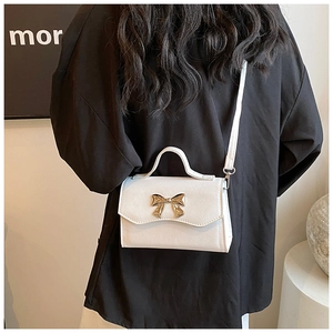 Close-up of white cross-grain leather crossbody bag with a golden metal bow buckle